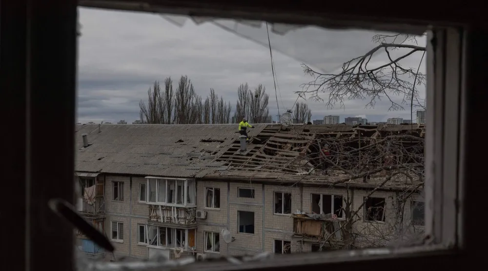 عمال يزيلون الأنقاض من سطح مبنى سكني متضرر بشدة عقب غارة جوية بطائرة مسيرة في كييف (أ.ف.ب)