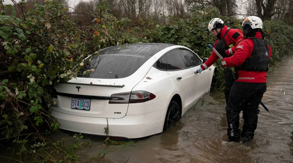 عناصر من إدارة الطوارئ الأميركية يفحصون سيارة «تسلا» خالية خلال فيضان غرين ريفر في واشنطن (رويترز)
