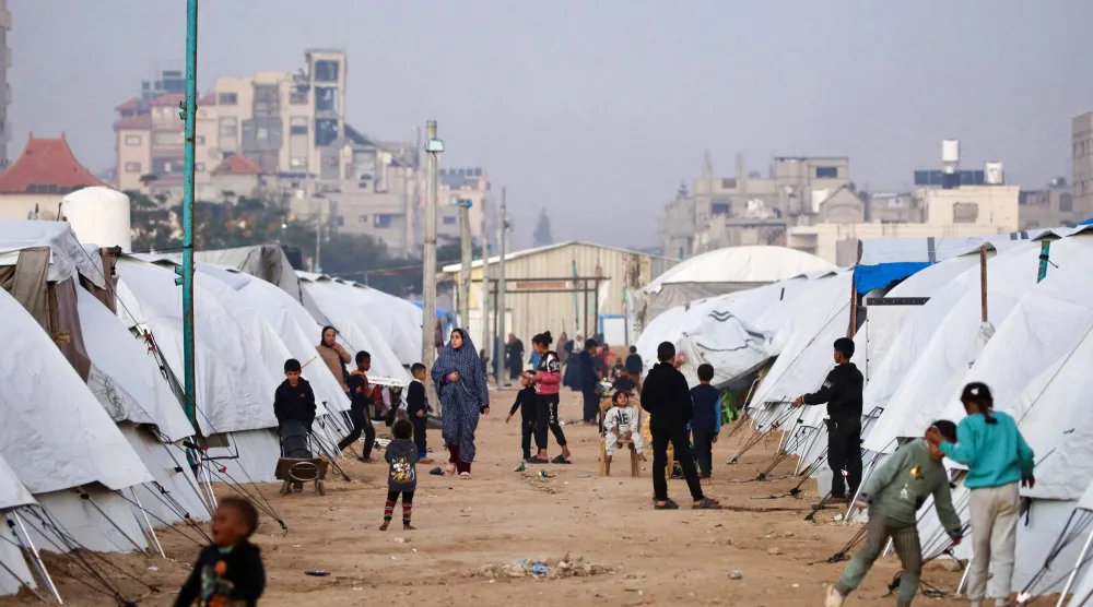 فلسطينيون يسيرون وسط الملاجئ في مخيم النصيرات للنازحين الفلسطينيين بغزة (أ.ف.ب)