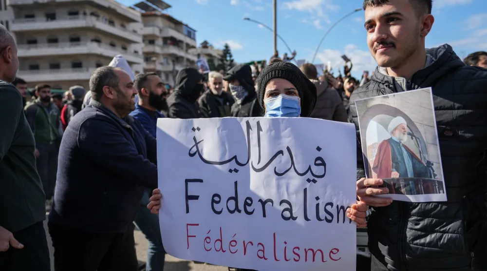 متظاهر في مدينة اللاذقية يحمل لافتة تطالب بفيدرالية في الساحل السوري في حين يتجمع أفراد من «الطائفة العلوية» للاحتجاج على تفجير مسجد حمص (إ.ب.أ)