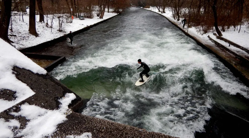 (FILES) Surfers ride the Eisbach (ice creek) wave during freezing conditions on the Isar River in the English Garden in Munich, southern Germany on January 4, 2017. (Photo by Mark RALSTON / AFP)