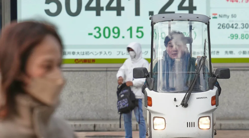 مشاة يمرون أمام شاشة إلكترونية تعرض حركة الأسهم في وسط العاصمة اليابانية طوكيو (أ.ب)