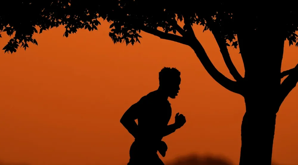 A man is silhouetted against the sky at sunset as he jogs in a park at the close of a hot summer day, Aug. 1, 2022, in Kansas City, Mo. (AP Photo/Charlie Riedel, File)