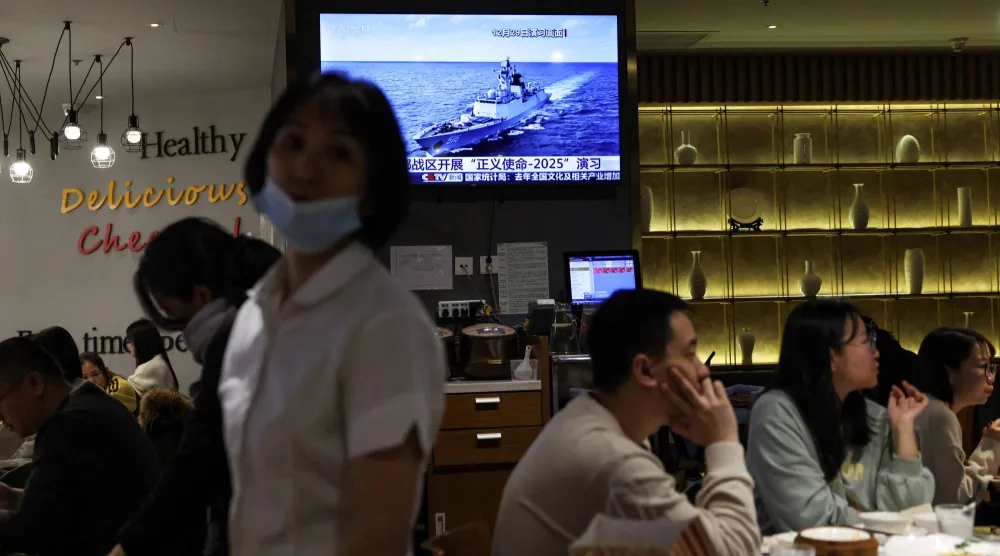 يتناول رواد مطعم في بكين-الصين الطعام بالقرب من شاشة تلفزيون تعرض تقريراً إخبارياً عن مناورات «مهمة العدالة 2025» العسكرية الصينية حول تايوان (رويترز)