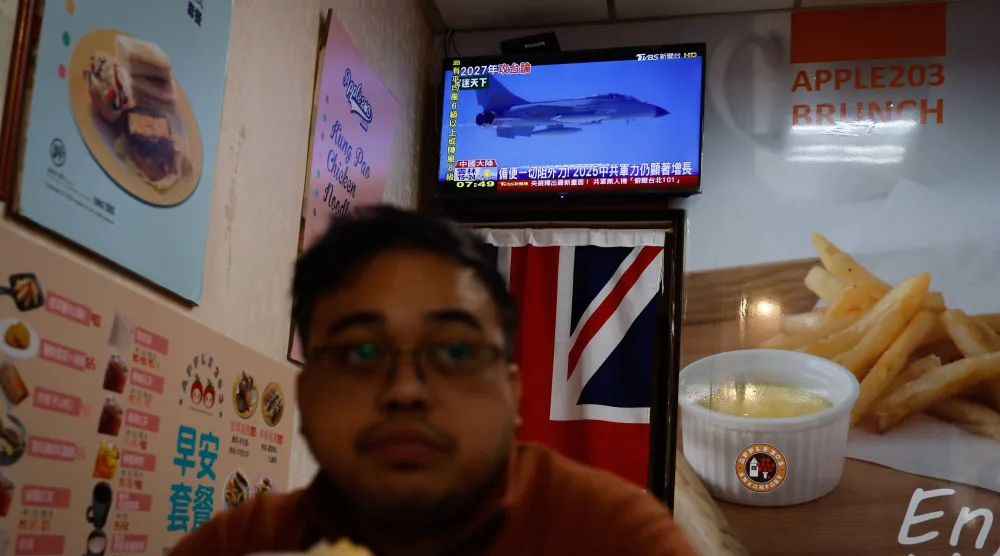 شخص يشاهد أخباراً عن إجراء الجيش الصيني تدريبات بالذخيرة الحية حول تايوان داخل متجر إفطار في تايبيه (إ.ب.أ)