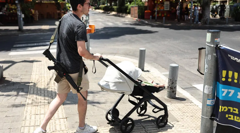 إسرائيلي مسلح يدفع عربة أطفال في تل أبيب (أ.ف.ب)