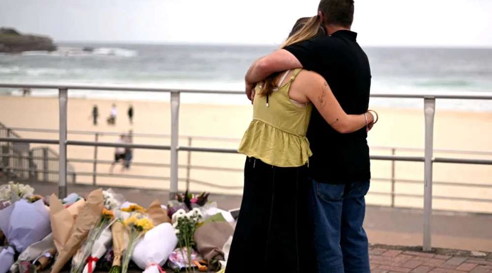 Sydney'deki Bondi Plajı'nda meydana gelen silahlı saldırıda hayatını kaybedenleri anmak için konulan çiçek yığınlarının yanında yas tutanlar birbirlerine sarılıyor ,16 Aralık