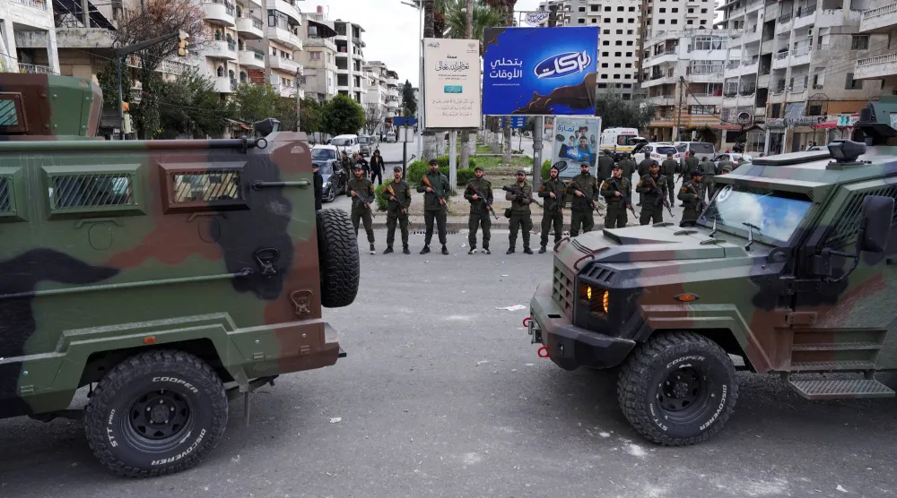 FILE PHOTO: Members of the Syrian Security forces stand guard near military vehicles on the day people protest in Latakia, Syria, December 28, 2025. REUTERS/Karam al-Masri/File Photo