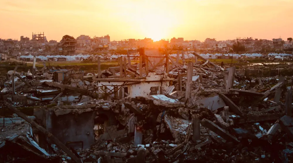 The sun sets behind the ruins of destroyed buildings in the Nuseirat refugee camp in the central Gaza Strip on December 31, 2025. (AFP)