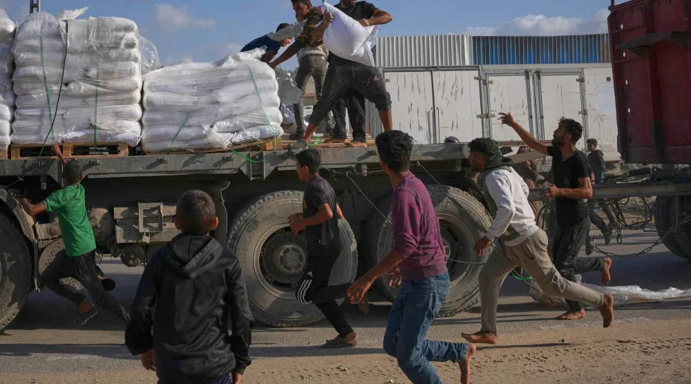 فلسطينيون يحاولون اقتناص أجولة طحين (دقيق) من شاحنة تحمل مساعدات من «برنامج الأغذية العالمي» خلال سيرها في دير البلح بوسط قطاع غزة (أ.ب)