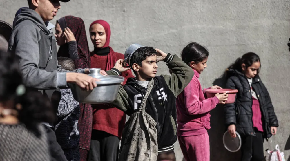 فلسطينيون في مخيم النصيرات وسط قطاع غزة ينتظرون تلقي وجبات الطعام يوم الثلاثاء (د.ب.أ)