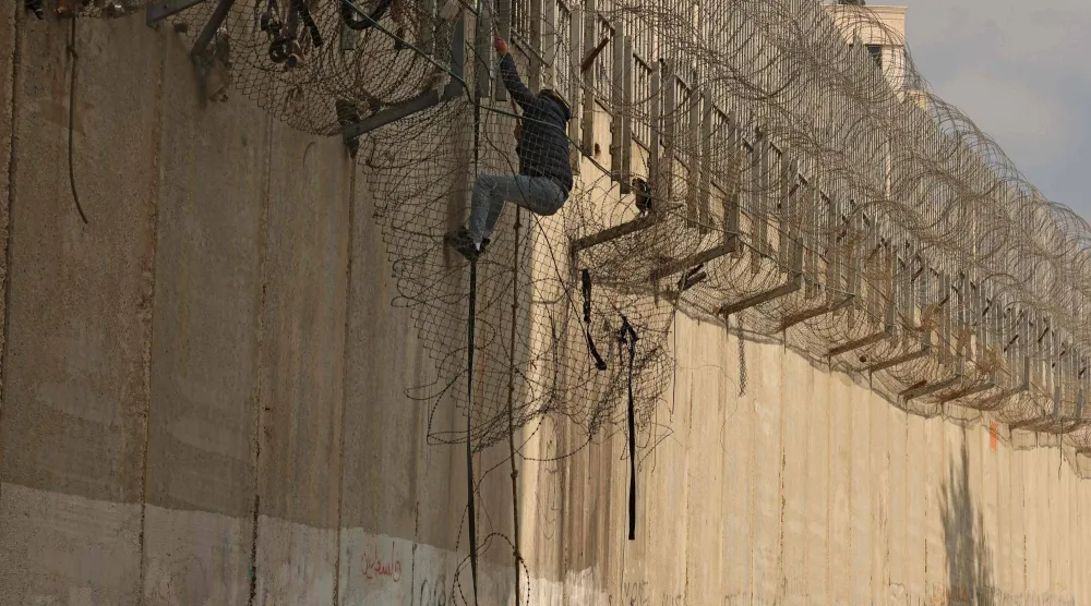 فلسطيني يتسلق جدار الفصل الإسرائيلي الذي يفصل الضفة الغربية عن القدس السبت (أ.ف.ب)