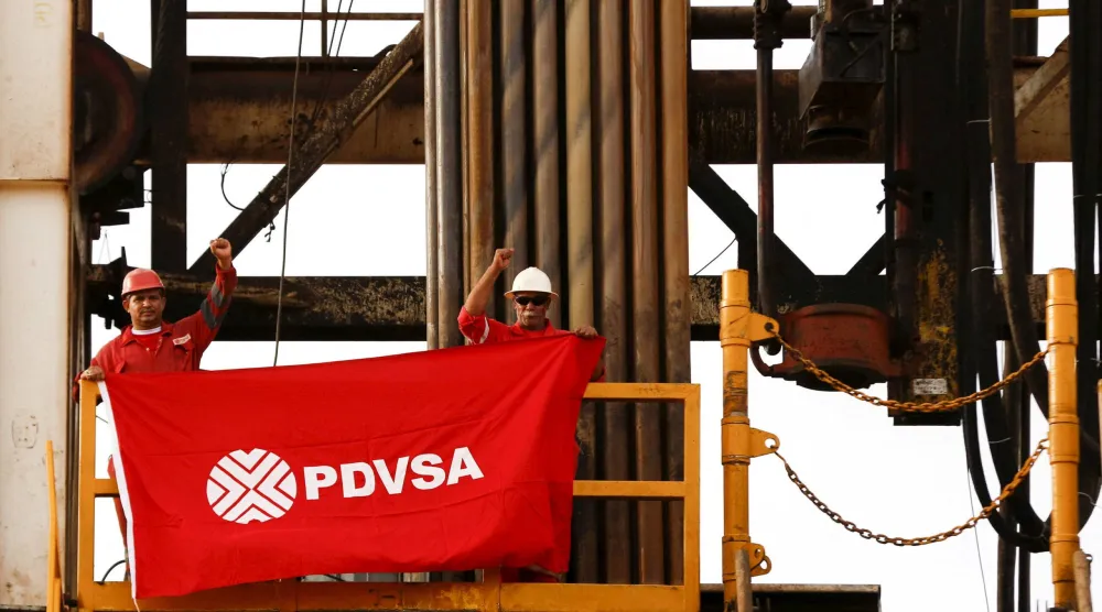 عاملان في حقل نفط يرفعان علماً يحمل شعار شركة النفط الحكومية الفنزويلية PDVSA (رويترز)