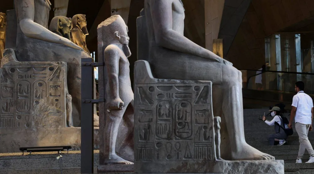 سائحة تلتقط صوراً لتماثيل معروضة داخل المتحف المصري الكبير والذي جذب العديد من السياح في 2025 (رويترز)