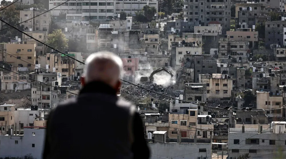 سكان مخيم نور شمس يشاهدون منازلهم تُهدم عشية رأس السنة الميلادية على يد حفارة عسكرية إسرائيلية في المخيم شرق مدينة طولكرم شمال الضفة الغربية المحتلة (أ.ف.ب)