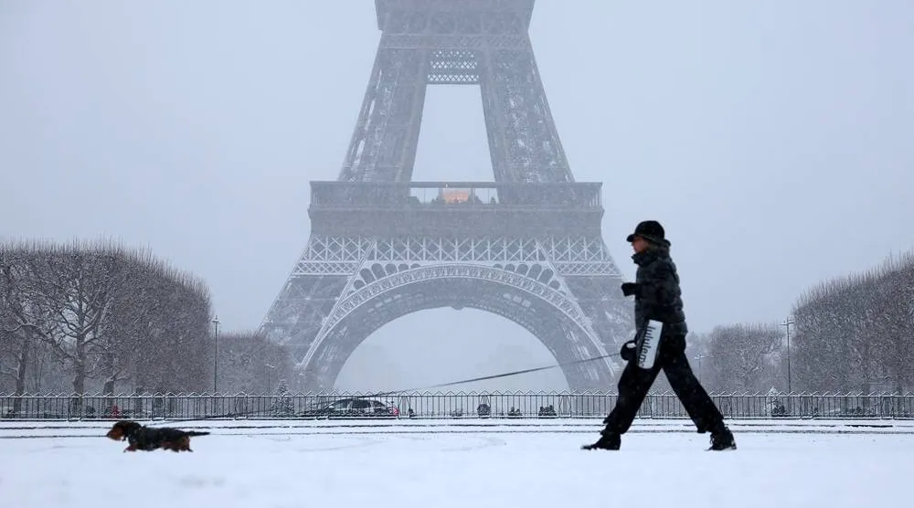 A woman walks her dog in a snow-covered area in front the Eiffel Tower in Paris, as winter weather with snow and cold temperatures hits a large part of the country, France, January 5, 2026. (Reuters) 