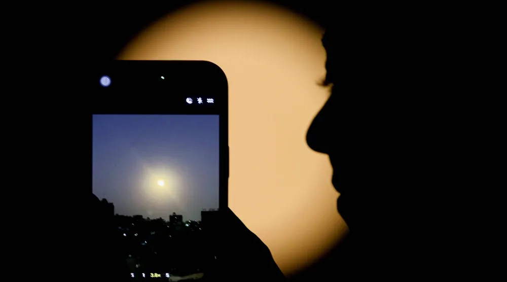 امرأة تستخدم هاتفها الذكي لتصوير قمر الذئب أول قمر عملاق في عام 2026 وهو يضيء سماء القاهرة ليلاً (رويترز)