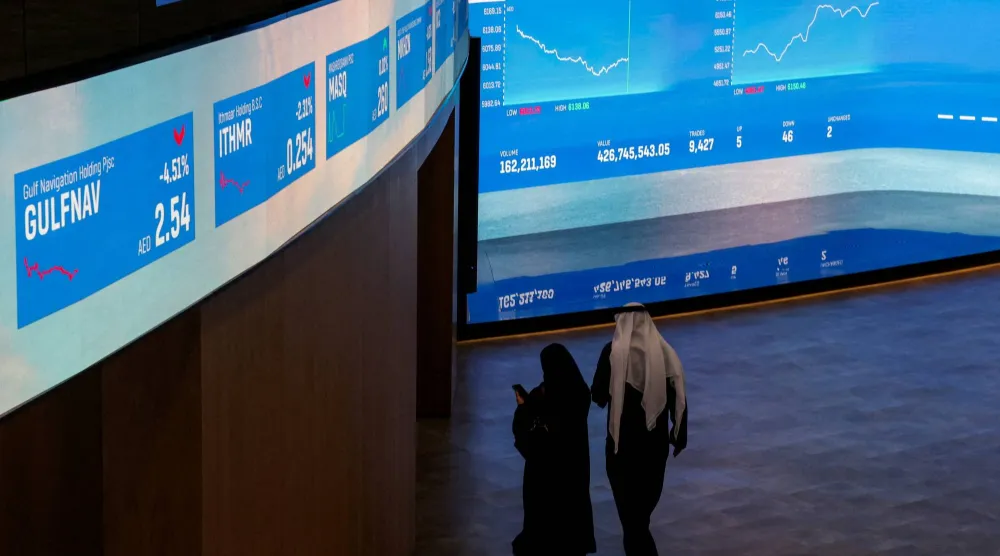 شخصان يسيران بالقرب من شاشات عرض معلومات الأسهم في سوق دبي المالي (رويترز)