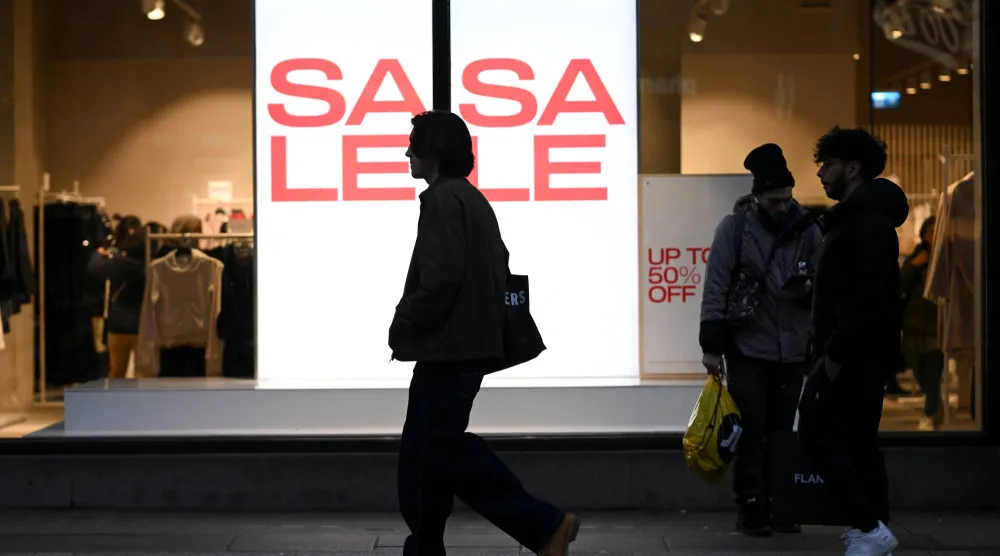 يمرّ أشخاص بجانب متجر يعرض لافتات تخفيضات في شارع أكسفورد بلندن (رويترز)