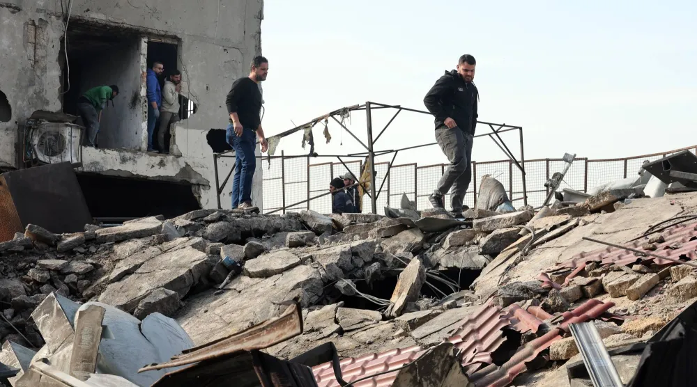 مواطنون يعاينون المبنى الذي استهدف فجراً بغارة إسرائيلية في الغازية قرب مدينة صيدا (إ.ب.أ)
