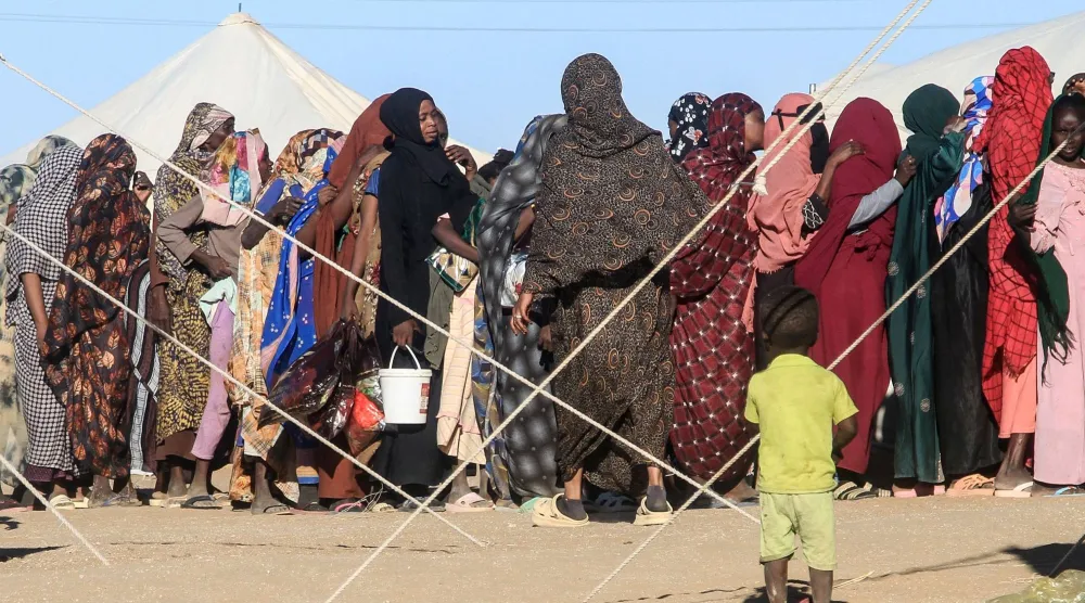 طفل ينظر إلى نساء يصطففن لتلقي المساعدات في مخيم ببلدة الدبة شمال السودان يوم 15 نوفمبر (أ.ف.ب)