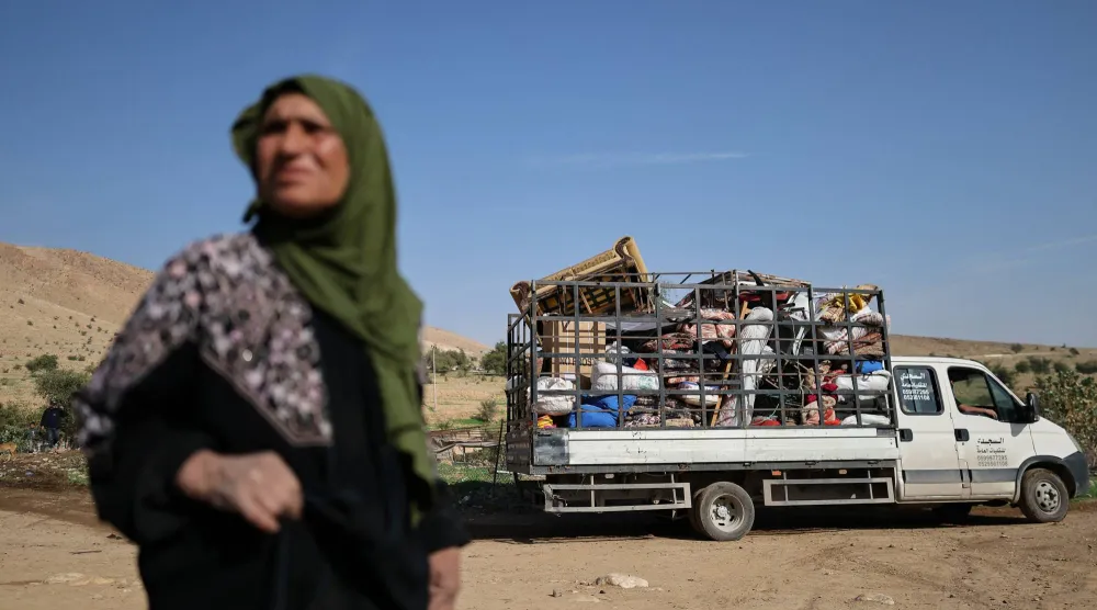 فلسطينية تقف قرب شاحنة تنقل متعلقات عائلاتها التي نزحت قسراً مع عائلات أخرى يوم الخميس من منطقة العوجا البدوية قرب أريحا بالضفة الغربية بعد تصاعد هجمات المستوطنين الإسرائيليين (رويترز)
