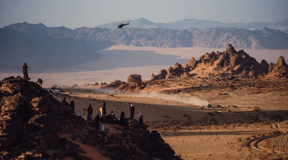 سيارة أحد المتسابقين تشق طريقها في حين يراقب عشاق الرالي المشهد من فوق إحدى الهضاب (الشرق الأوسط)