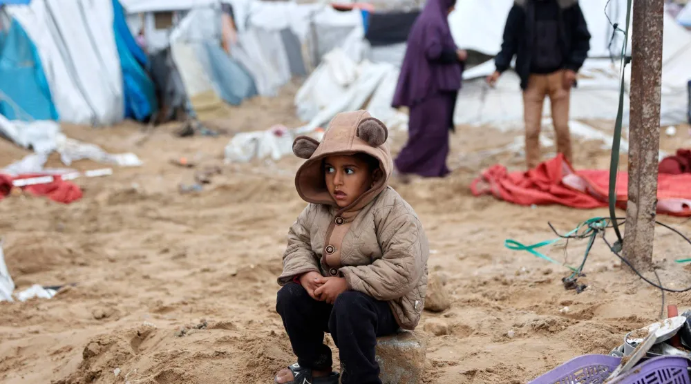 طفل فلسطيني يجلس على حجر فيما عائلته تعيد تنظيم الخيمة التي تؤويهم بعد قصف إسرائيلي استهدف مخيم الشاطئ للاجئين بمدينة غزة (أ.ف.ب)