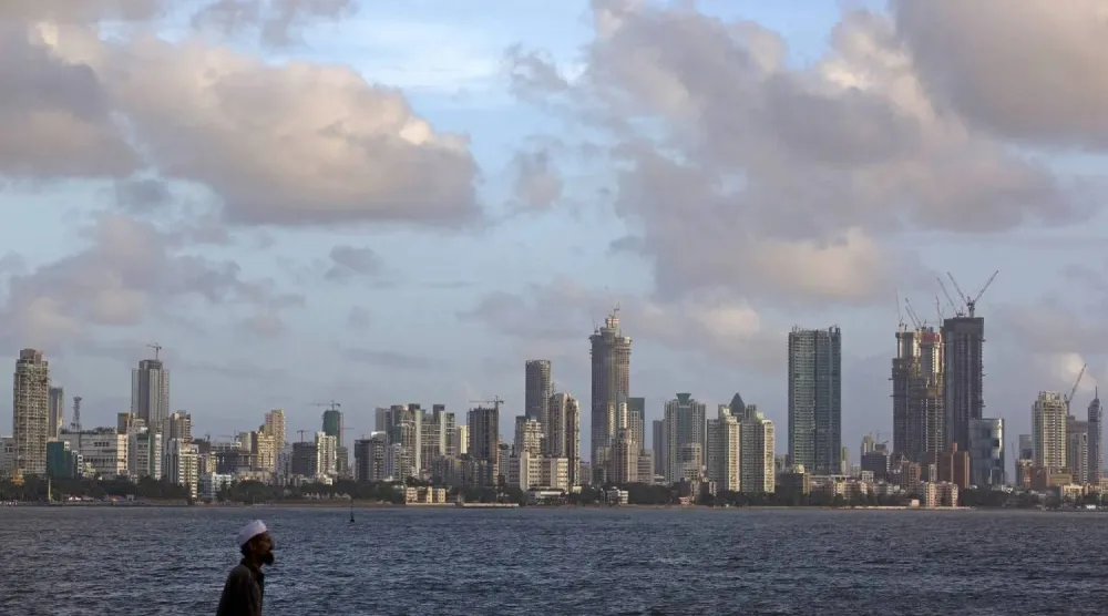 رجل يمشي على الواجهة البحرية بينما تظهر بعض الغيوم المتفرقة في أفق مومباي (رويترز)