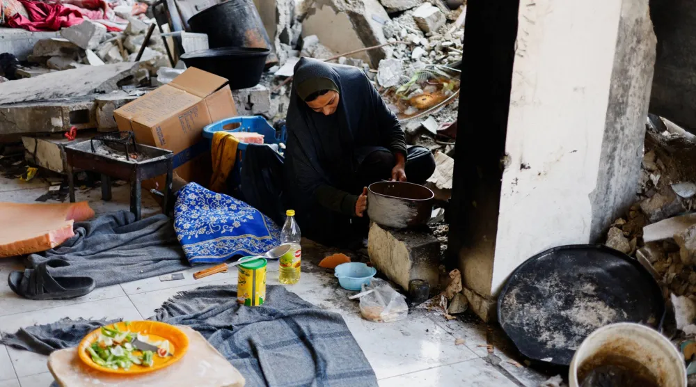 فلسطينية تطهو الطعام بين حطام منزلها في غزة (رويترز)