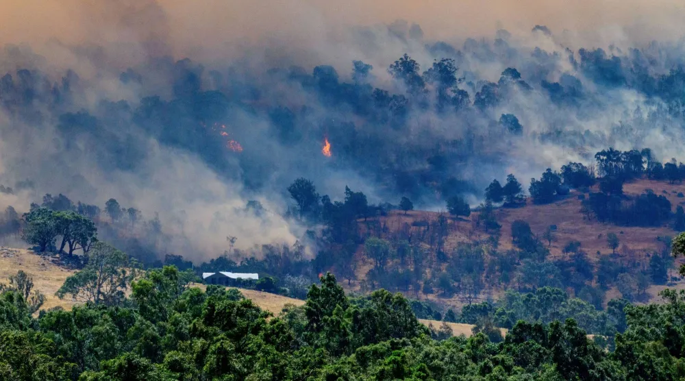 Smoke rises from a burning forest on a hillside behind a home near Longwood as bushfires continue to burn under severe fire weather conditions in Longwood, Victoria, Australia, January 9, 2026. AAP/Michael Currie via REUTERS 