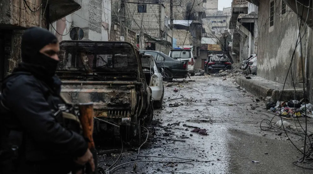 جندي سوري يقف أمام سيارة محترقة في حي الشيخ مقصود في حلب جراء الاشتباكات مع «قسد» (د.ب.أ)