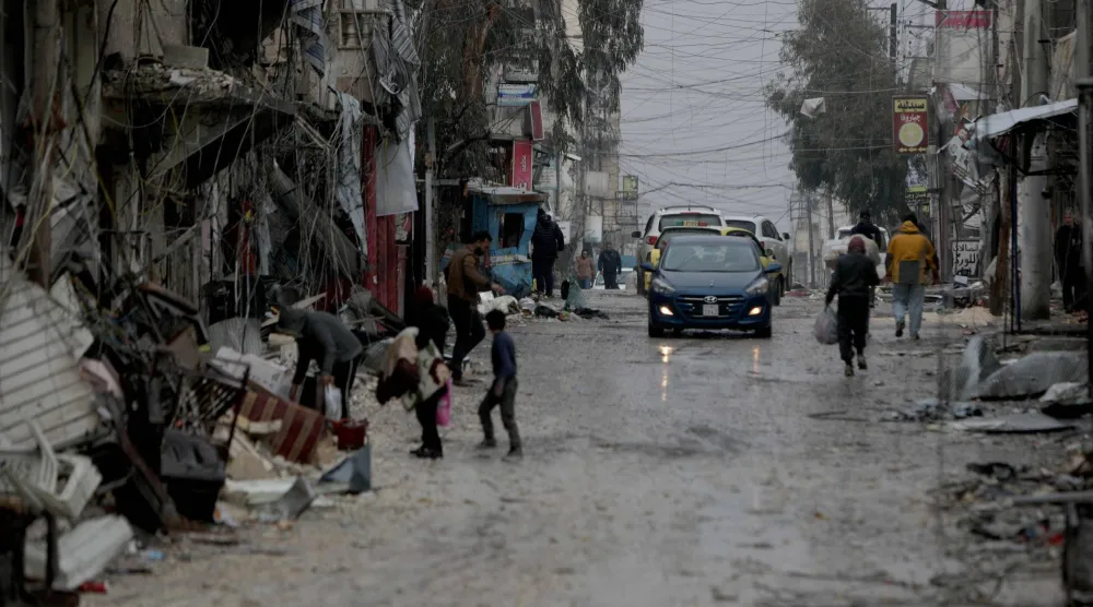 People walk down a street as a car drives by following a ceasefire which ended days of fighting between Syrian security forces and Kurdish fighters in the Kurdish-majority Sheikh Maqsoud neighborhood, of the northern city of Aleppo on January 11, 2026. (AFP)