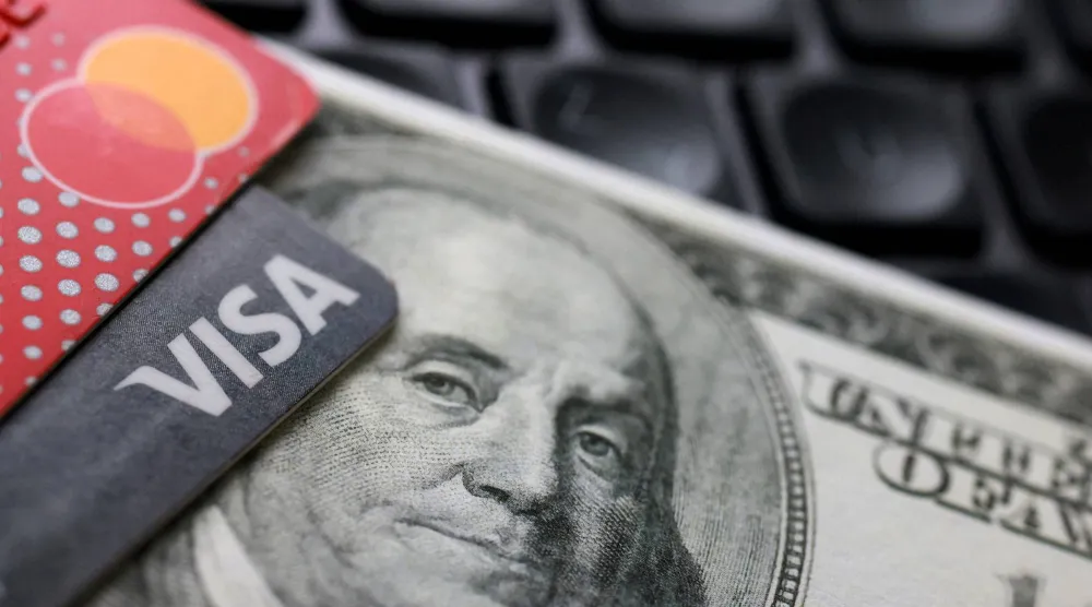 ورقة نقدية بالدولار الأميركي وبطاقتا فيزا وماستركارد موضوعة على لوحة مفاتيح في هذه الصورة التوضيحية (رويترز)
