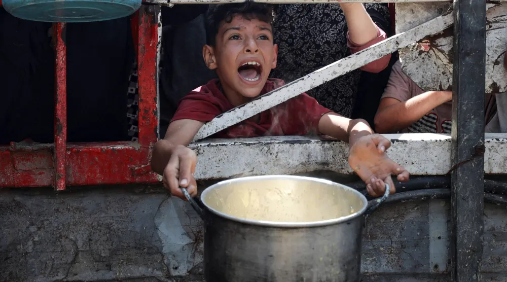 طفل فلسطيني يصرخ بانتظار الحصول على الطعام من مطبخ خيري وسط أزمة الجوع في مدينة غزة (رويترز)