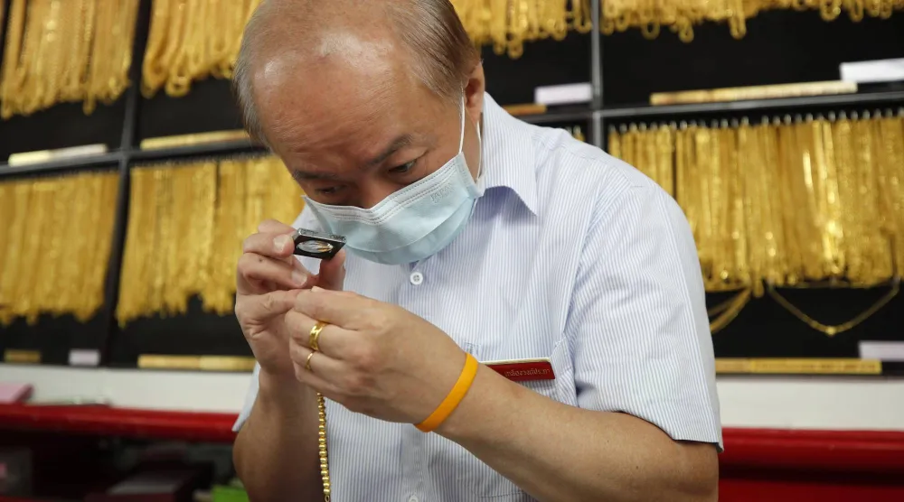 صائغ يفحص الحلي الذهبية في متجر للذهب في بانكوك (إ.ب.أ)