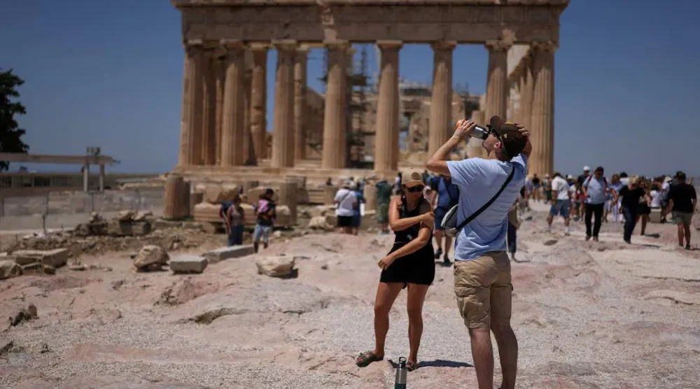 سائح يشرب الماء خلال زيارته لمعبد البارثينون في ظل موجة حرّ تضرب أثينا في اليونان يوم 27 يونيو 2025 (رويترز)