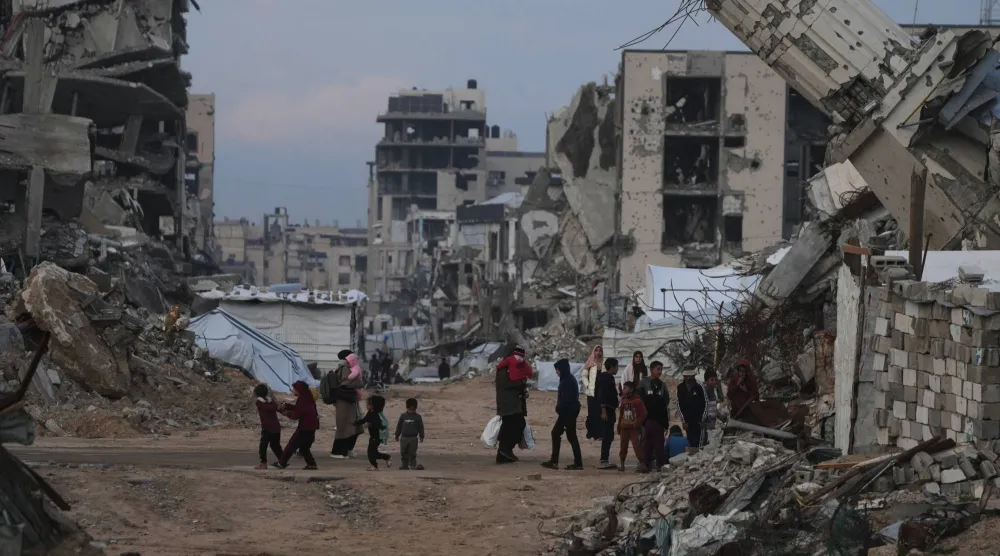  فلسطينيون يسيرون بجانب مبان دمرتها غارات إسرائيلية في حي الزيتون بقطاع غزة (ا.ب)