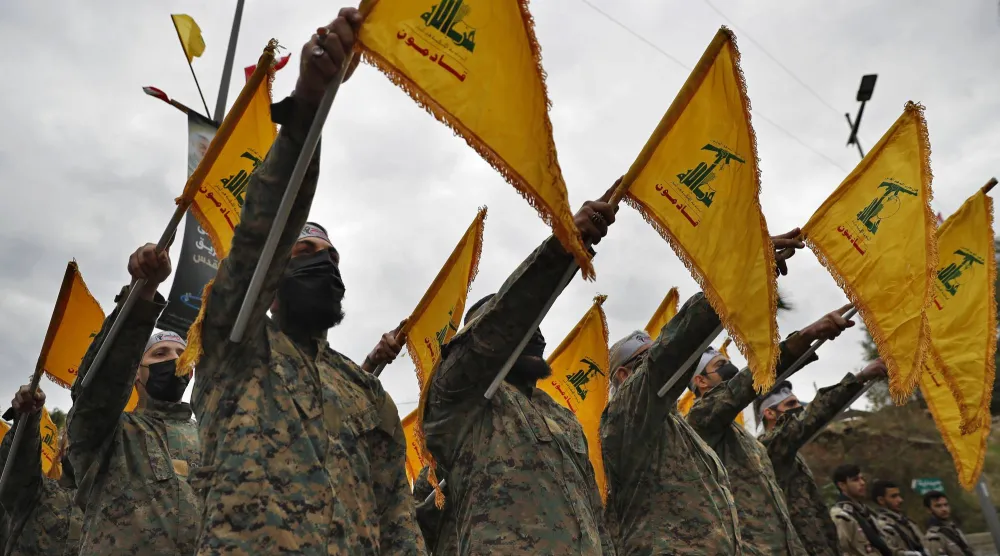 Hezbollah fighters hold their group's flag as they stand in front of a statue of Iranian General Qassem Soleimani and swear their oath of allegiance to him, during a ceremony to mark the second anniversary of his assassination, in the southern suburb of Beirut, Lebanon, Tuesday, Jan. 4, 2022. Soleimani was the head of Iran's Quds force who was killed by a U.S. drone in Baghdad in January 2020. (AP Photo/Hussein Malla)