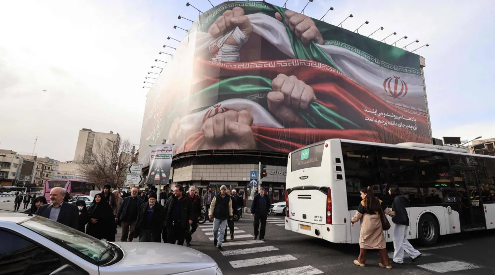 People walk past a large patriotic banner depicting the Iranian flag on Enghelab Square in Tehran on January 14, 2026.  (Photo by ATTA KENARE / AFP)