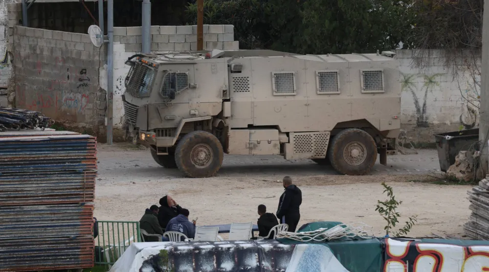 فلسطينيون يشاهدون آلية عسكرية إسرائيلية تنقل جنوداً إلى مخيم نور شمس قرب طولكرم بالضفة الغربية (إ.ب.أ)