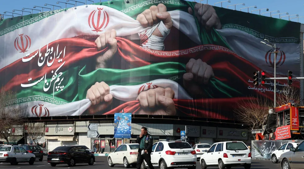 إيرانيون يسيرون بجوار لوحة إعلانية كُتب عليها باللغة الفارسية «إيران وطننا» بطهران (إ.ب.أ)