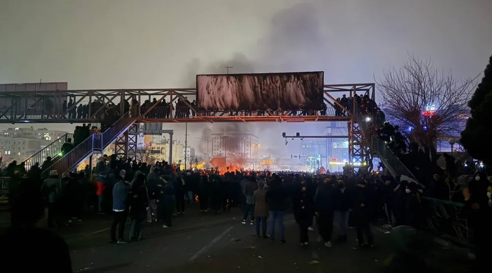 محتجون يحرقون لافتة معلقة فوق جسر للمشاة في حي بونك شمال غربي طهران الجمعة (تلغرام)