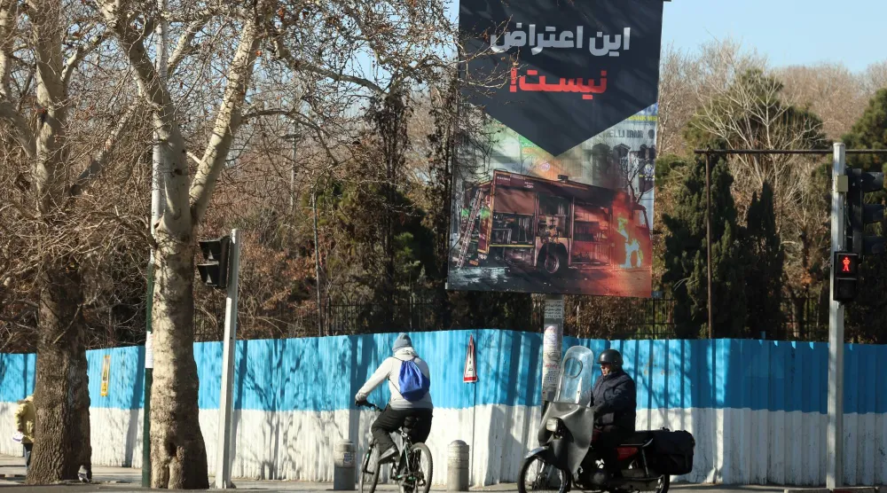 إيرانيون يسيرون بجانب لافتة مكتوب عليها باللغة الفارسية «هذا ليس احتجاجاً» في أحد شوارع طهران (إ.ب.أ)