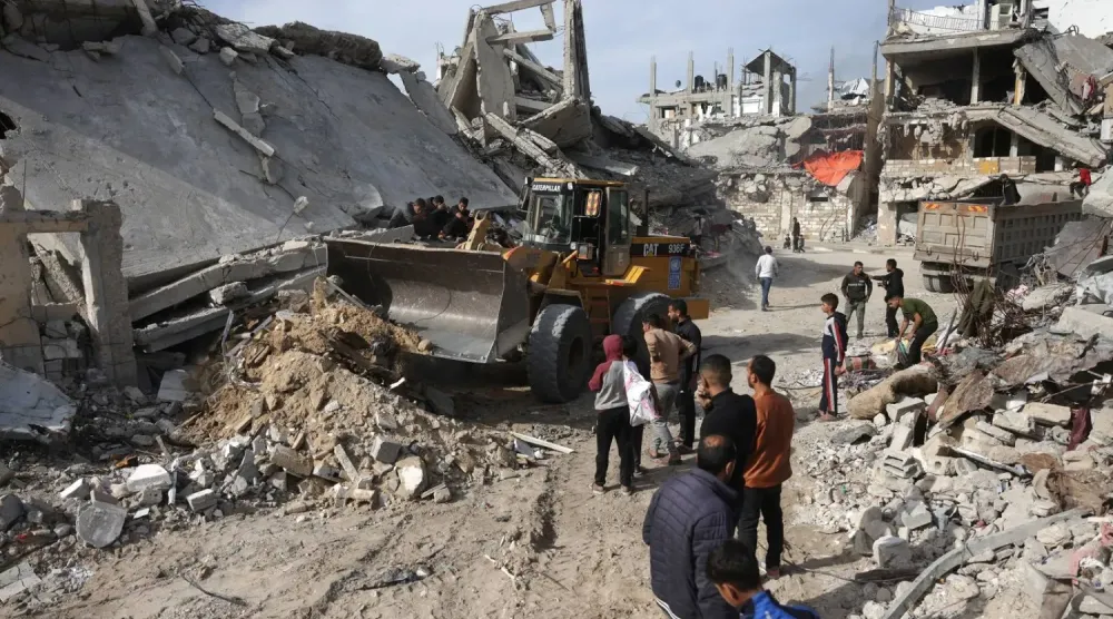 Gazze Şeridi'nin güneyindeki Han Yunus'ta yıkılmış binalar ve evlerden beton, metal ve moloz taşımak için kullanılan bir ekskavatör (AFP)