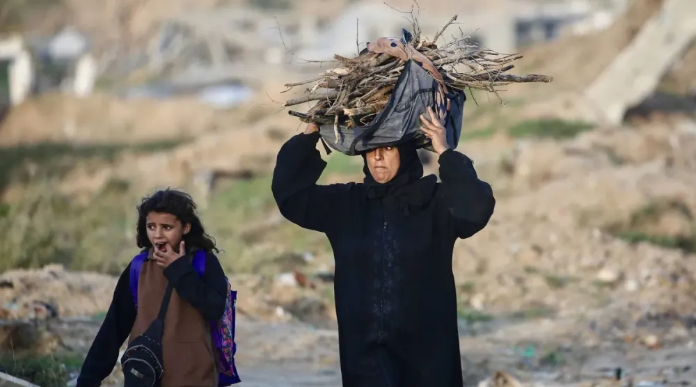 Filistinli bir kadın, Gazze Şeridi'nin merkezindeki Nuseyrat mülteci kampında ateş yakmak için odun taşıyor (AFP)