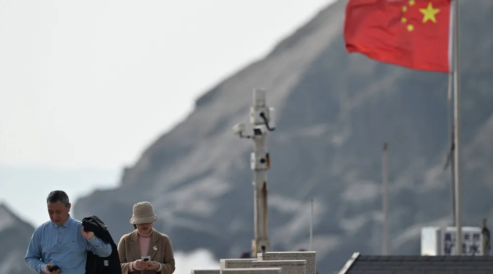يمرّ زوار بجوار نقطة مراقبة بالكاميرا (وسط) وعَلم صيني (يمين) في جزيرة بينغتان أقرب نقطة إلى تايوان بمقاطعة فوجيان شرق الصين (أ.ف.ب)