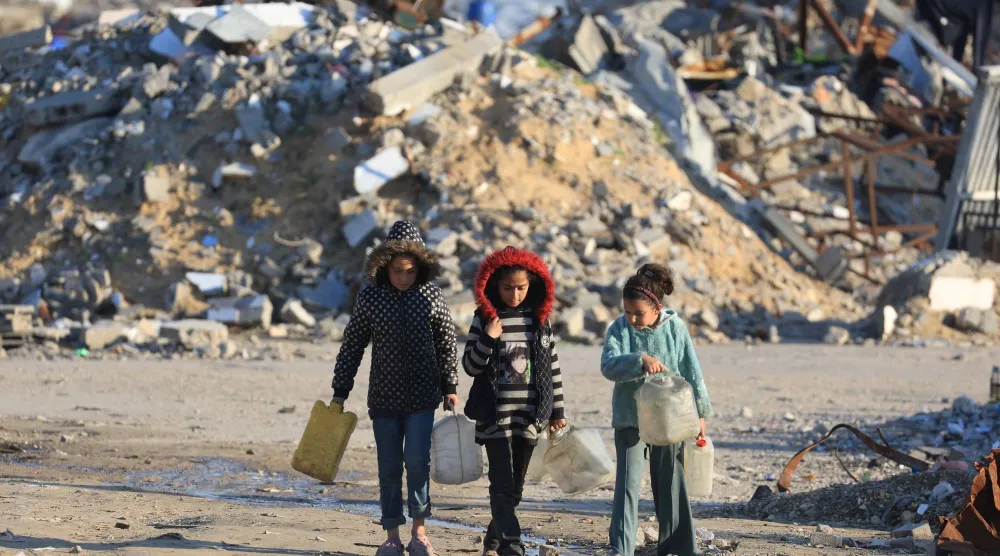 فتيات فلسطينيات يمررن بين أنقاض مبانٍ سكنية دُمرت خلال الحرب (رويترز)