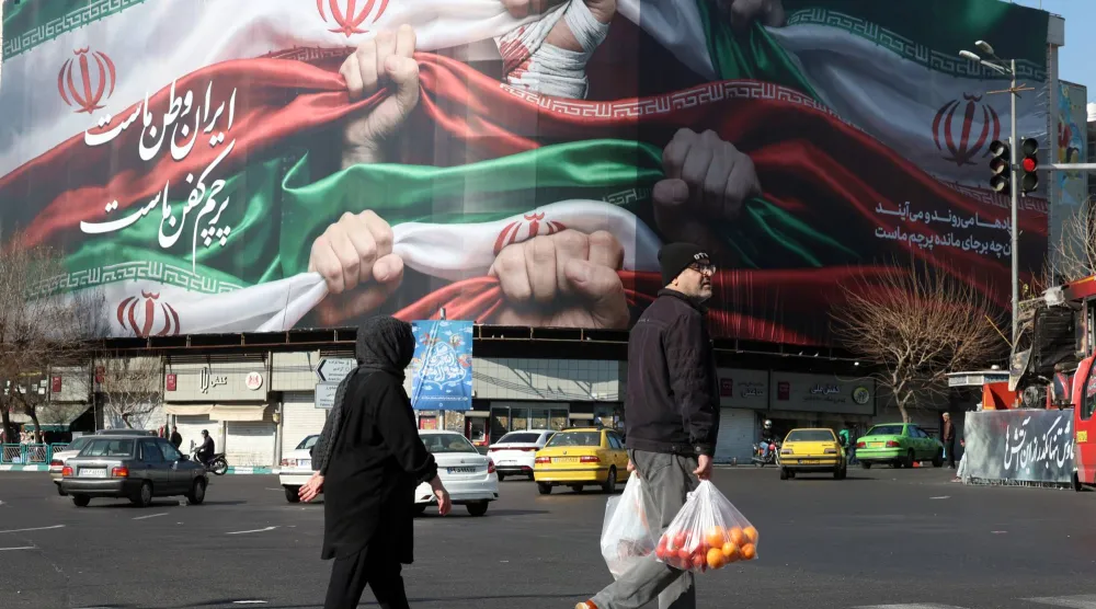 إيرانيون يسيرون بجوار لوحة إعلانية في متجر كُتب عليها باللغة الفارسية «إيران وطننا» بطهران (إ.ب.أ)