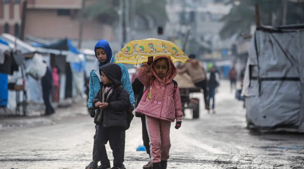 أطفال فلسطينيون في طريقهم لمدرسة في دير البلح بوسط قطاع غزة وسط موجة أمطار (أ.ف.ب)